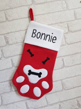 Load image into Gallery viewer, red felt Christmas stocking in the shape of a paw with a white felt top. Decorated with black glitter bones and a black glitter name across the top.