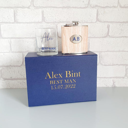 navy blue rectangular gift box with a square whisky glass and wooden hip flask with silver finishings. 