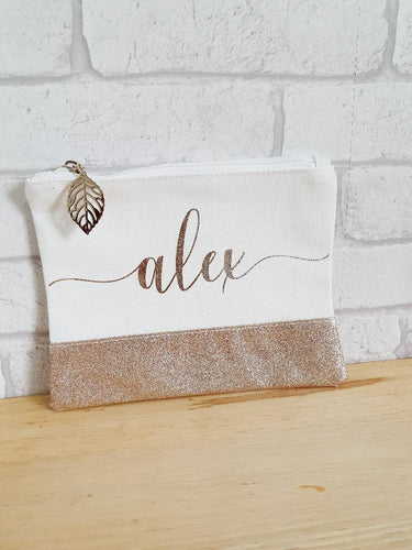 cream make-up bag with glitter gold panel along the bottom and matching gold name across the middle. A gold leaf zipper along the top
